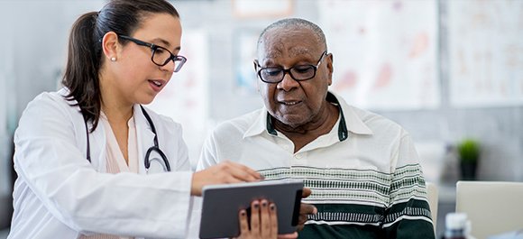 Doctor with elderly patient showing medical report on tablet device